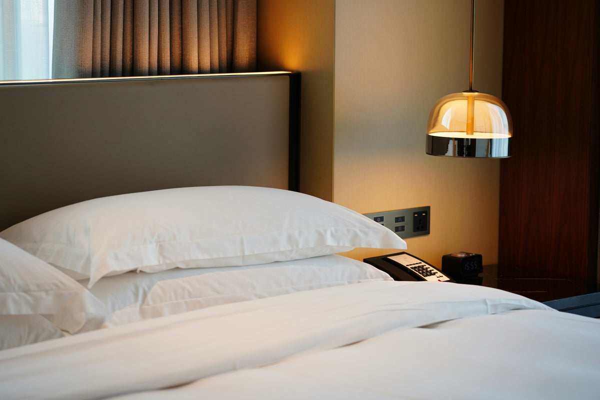 A hotel bed with crisp white linen in warm lamplight